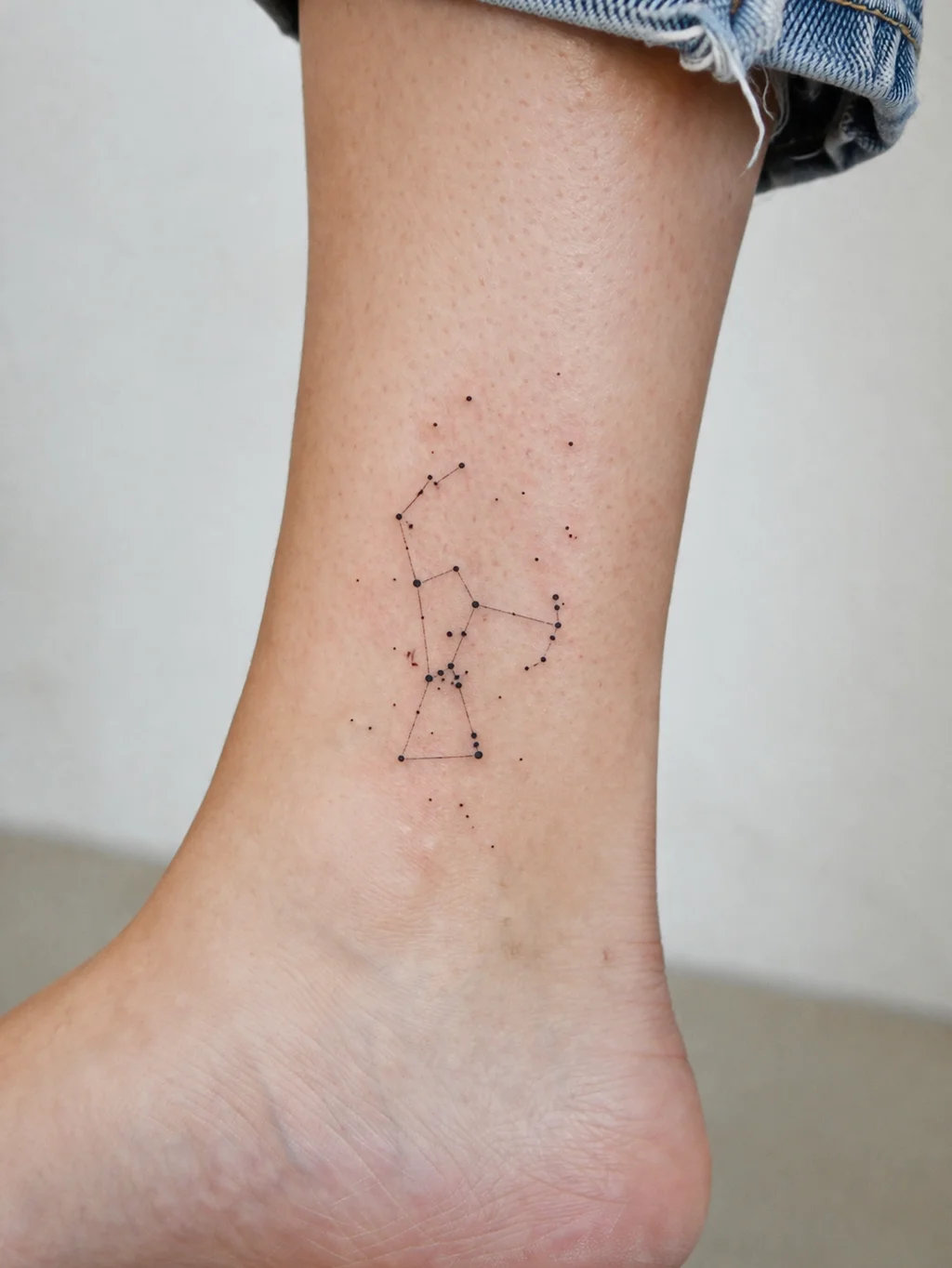 A delicate fine-line Orion constellation tattoo on a womans outer ankle with tiny star dots connected by thin lines